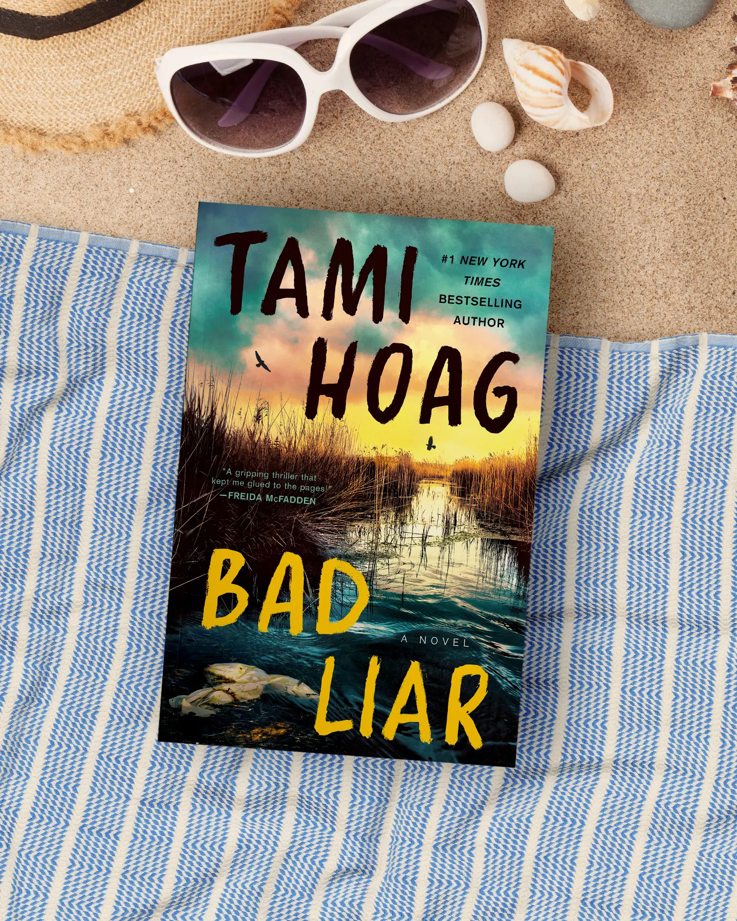 Book lying on beach towel with sunglasses and seashells.